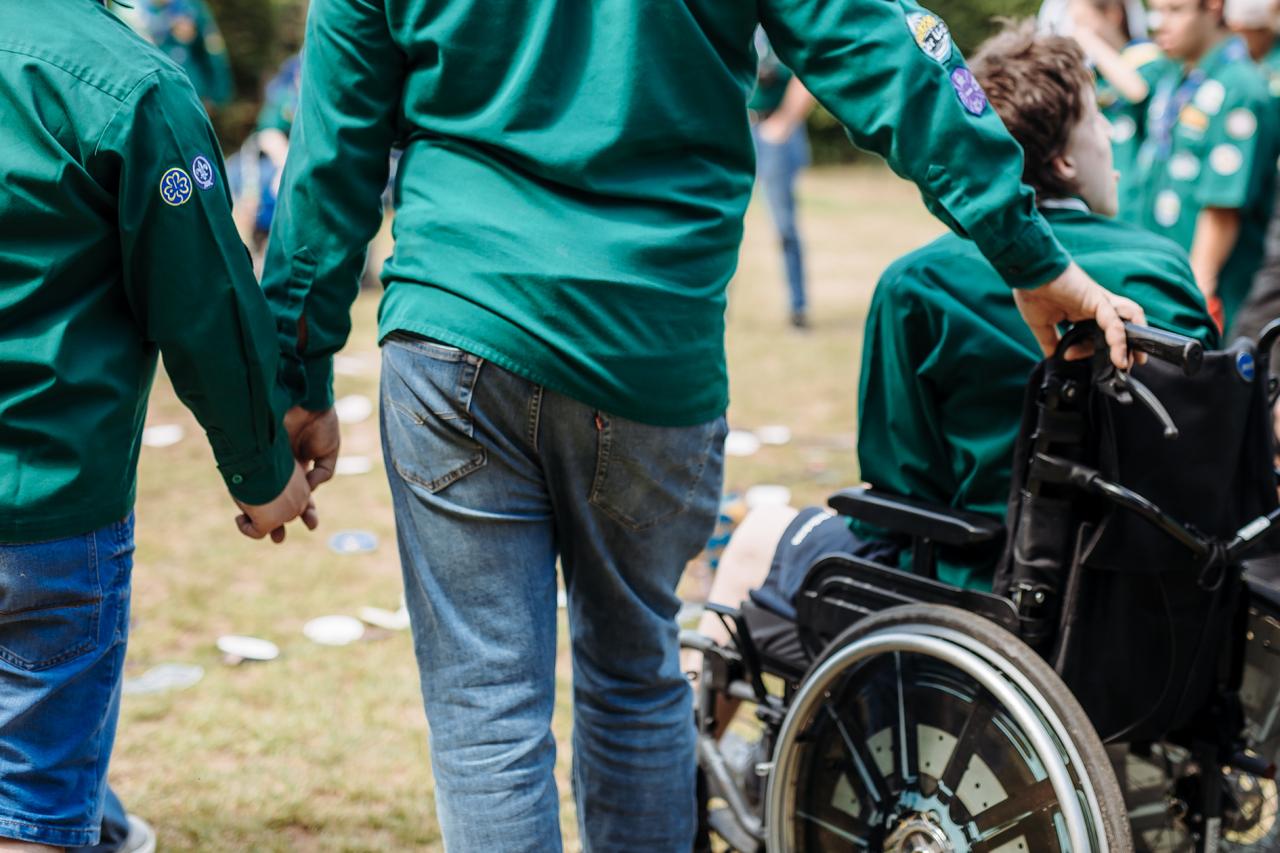 Un Scout tient la main d'un autre Scout et pousse une chaise roulante