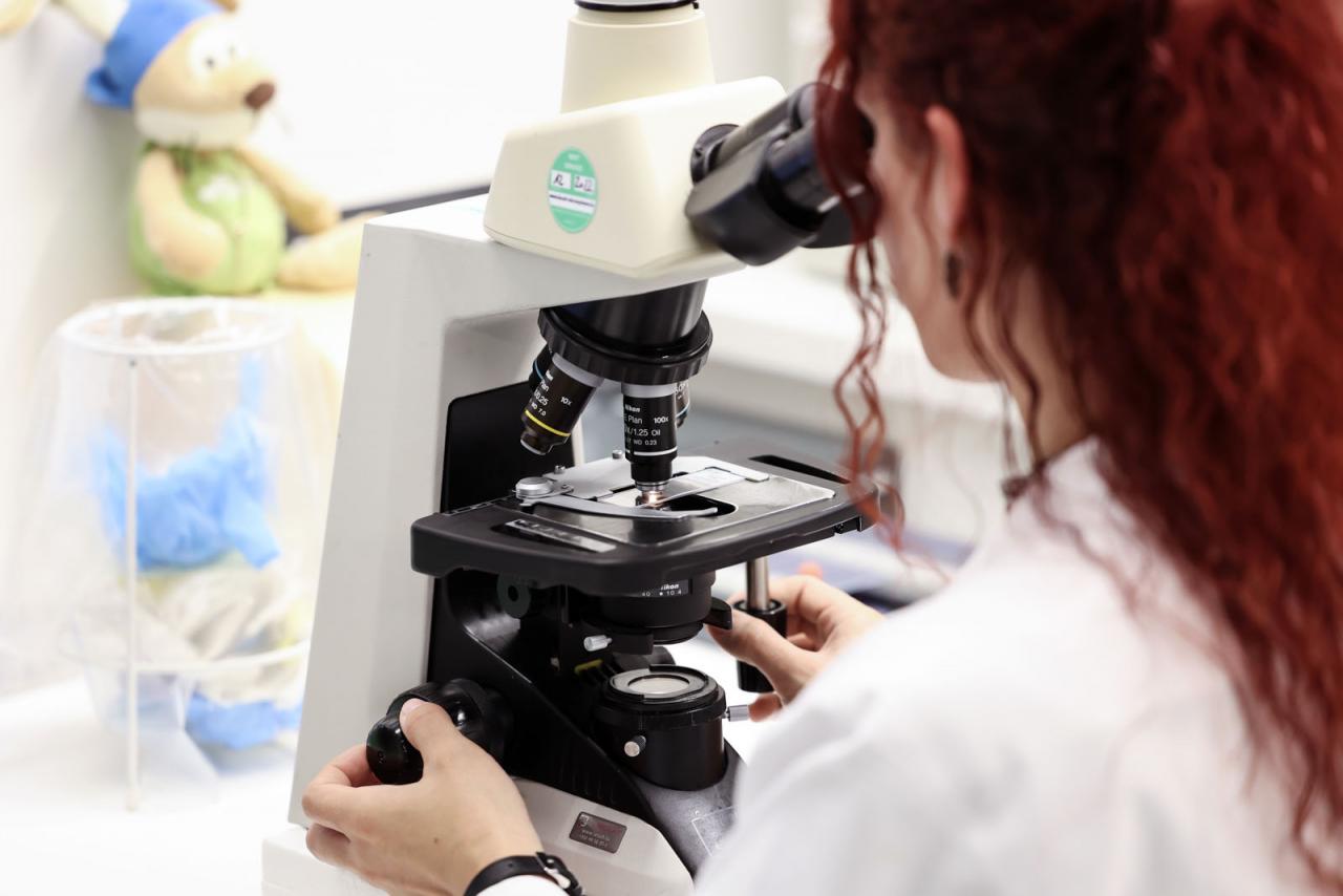 Une laborantine observe un échantillon à travers un microscope