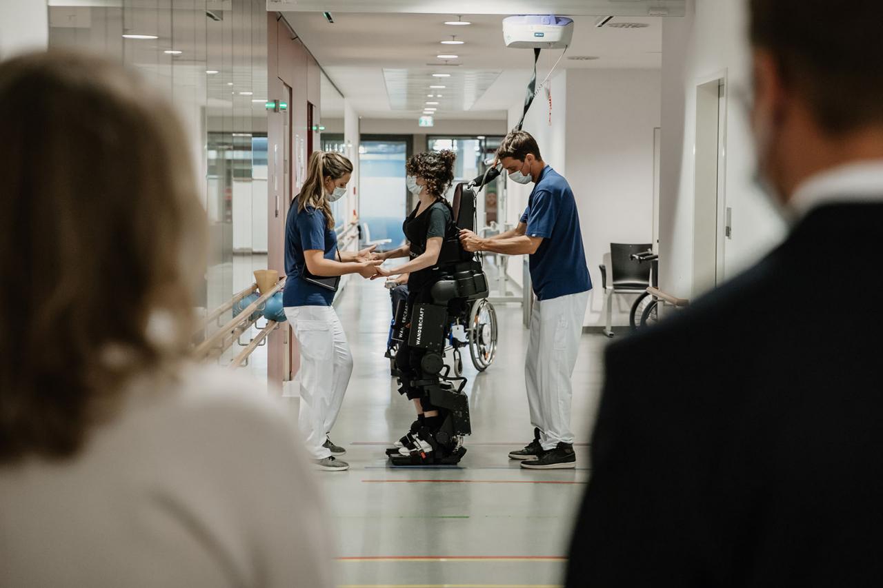 Dans le couloir, un patient marche à l'aide d'un exosquelette