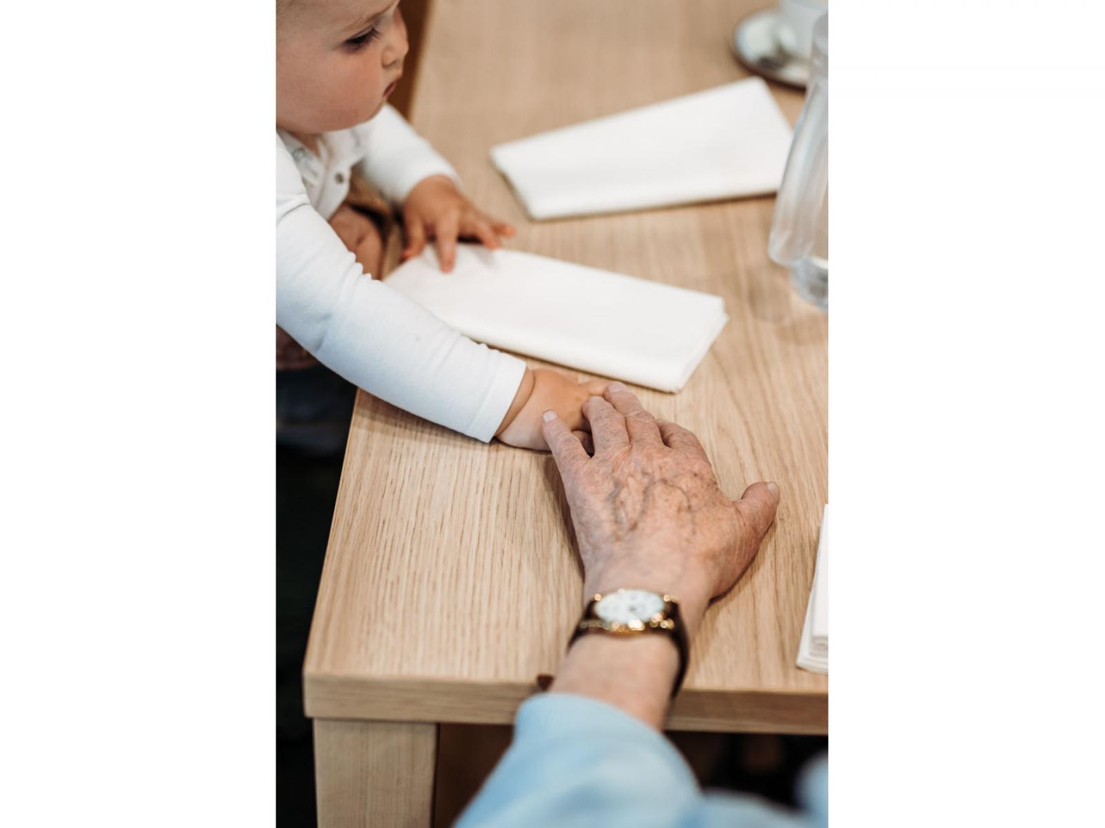 Une personne âgée donne la main au Prince Charles sur une table