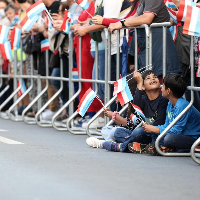 Deux enfants avec un drapeau luxembourgeois sont assis par terre et attendent la retraite aux flambeaux