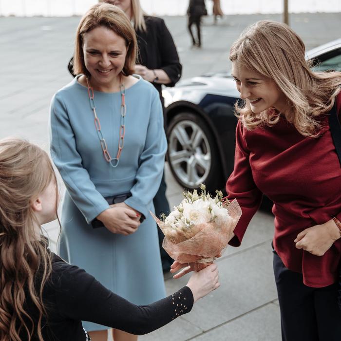 La Princesse est accueillie par une jeune fille avec un bouquet de fleurs