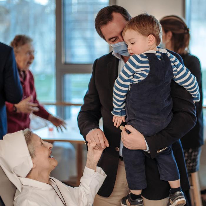 Le Prince Guillaume, avec le Prince Charles dans ses bras, salue une religieuse